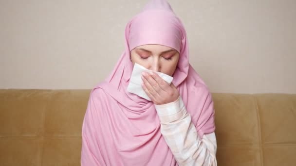 Mooie moslim vrouw in hijab hoest en bevriest terwijl zitten op de bank - Video