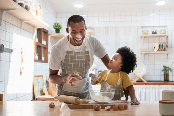 Cheerful smiling Black son enjoying playing with his father while doing bakery at home. Playful African family having fun cooking baking cake or cookies in kitchen together. Single Dad Lifestyle - Foto, Imagen