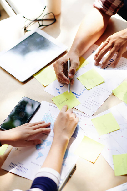 Руки бизнес-команды обсуждают отчеты и работу на встречах и написании ключевых слов на желтых наклейках - Фото, изображение