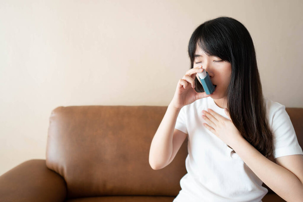 Nuori aasialainen nainen, joka käyttää sinistä astmainhalaattoria astmakohtaukseen. Lääkevalmisteita käytetään hengityksen vinkumisen ja astman tai keuhkoahtaumataudin ehkäisyyn ja hoitoon. Terveydenhuolto. - Valokuva, kuva