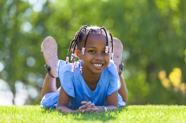 Outdoor portrait of a cute young black girl  lying down on the g - Zdjęcie, obraz