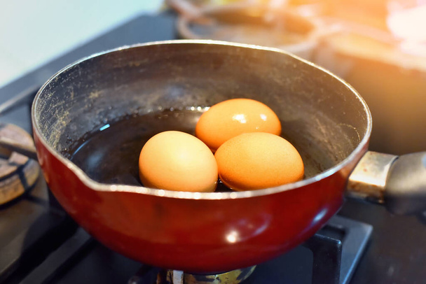 Яйца, кипящие в воде на газовой плите с солнечным светом. Изображение есть шум, Мягкий фокус. - Фото, изображение