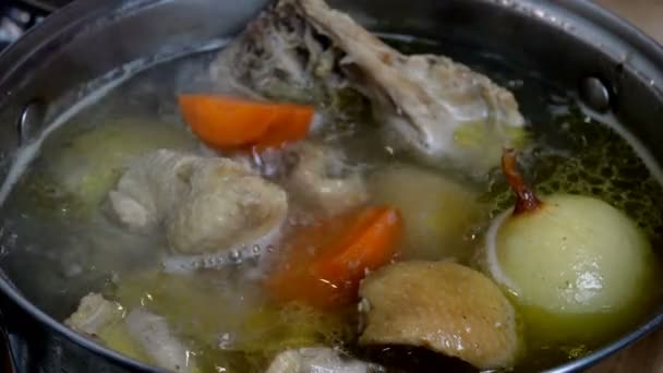 Főzés forró vízben zsíros csirkeleves húsból és csontokból, hagymával és sárgarépával leves elkészítéséhez, serpenyőben. Házi konyha. Közelkép. - Felvétel, videó