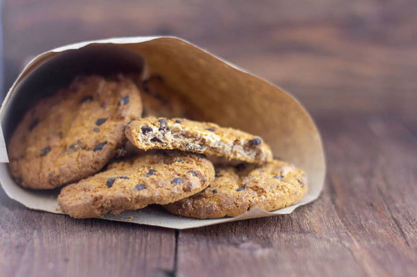 Köstliche Haferflocken-Kekse mit Schokoladenstücken in Packpapier auf Holzgrund - Foto, Bild