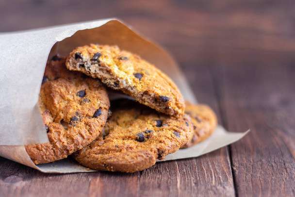 Köstliche Haferflocken-Kekse mit Schokoladenstücken in Packpapier auf Holzgrund - Foto, Bild