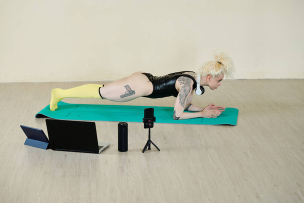 Fit forte jeune femme debout en position de planche sur le tapis en classe de danse lors de la conduite de cours en ligne pour les abonnés - Photo, image