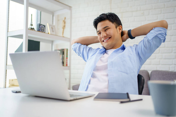 Les jeunes hommes asiatiques se détendent et travaillent à leur bureau. Il a souri en lisant l'écran de l'ordinateur. - Photo, image