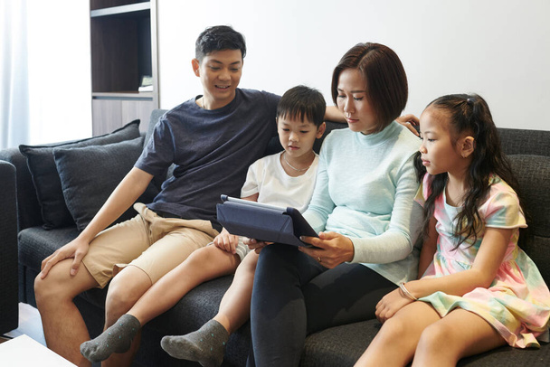 アジアの家族は自宅でソファに休んで、タブレットコンピュータで漫画や映画を見て - 写真・画像