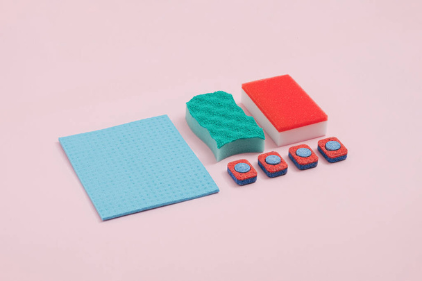 食器洗い機のタブレット、カラフルなスポンジとパステルカラーの背景に青の布で作成された近代的な春のクリーニングの配置。創造的で流行の平らなレイアウト. - 写真・画像