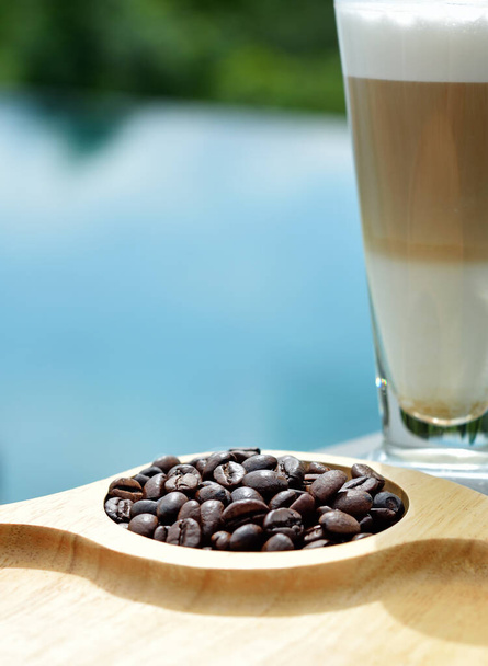 Roasted coffee beans on wooden tray with latte coffee at swimming pool - Photo, Image