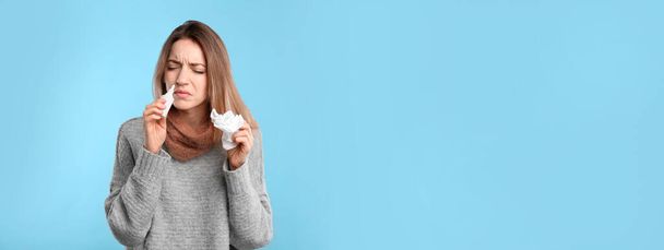 Sick young woman using nasal spray on light blue background - Photo, Image