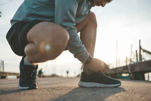 closeup of man tying shoe laces on the road before running in sunset. Sport and workout concept. - Photo, Image