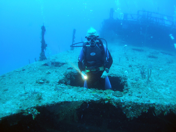 Mergulhador que aparece através do buraco no naufrágio Halliburton, Utila
 - Foto, Imagem