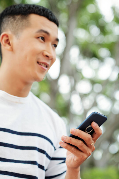 Азіатський молодий чоловік користується своїм мобільним телефоном під час прогулянки надворі. - Фото, зображення