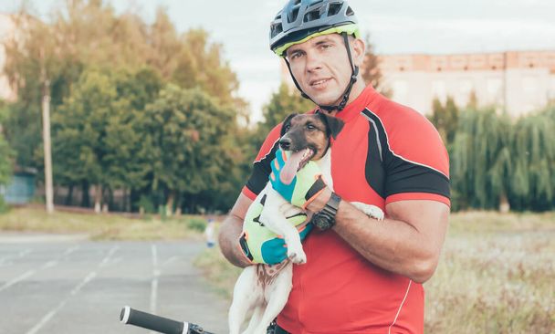 sportovní muž sedí na kole a drží psa ve svých rukou ve městě na stadionu - Fotografie, Obrázek