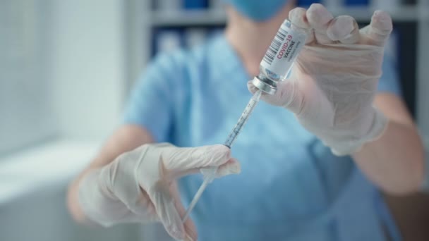 Zamaskowany lekarz z bliska trzyma strzykawkę i butelkę szczepionki w szpitalu, ręce w rękawiczkach ochronnych - Materiał filmowy, wideo