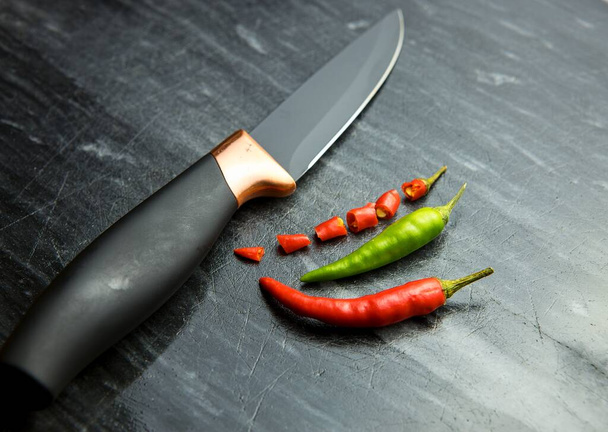 Červené a zelené chilli papričky a jeden plátky chilli paprika a nůž na černém pozadí - Fotografie, Obrázek