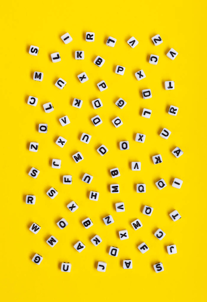 Weiße Würfel mit zufällig verstreuten Buchstaben auf gelbem Hintergrund. Das Bild kann für viele Zwecke verwendet werden, Buchumschläge oder Konzepte in Bezug auf Grammatik und Typografie. - Foto, Bild