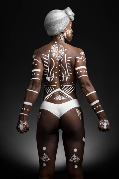 slim body detail of an african american woman only with underwear standing on her back, with body paint, short hair, studio with gray background - Fotoğraf, Görsel