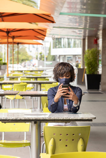 restaurant à l'extérieur avec une femme aux cheveux courts travaillant avec son téléphone portable en attendant à la table, portant du maquillage et des vêtements décontractés, style de vie en ville - Photo, image