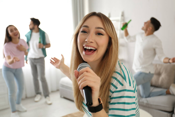 Young woman singing karaoke with friends at home - Zdjęcie, obraz