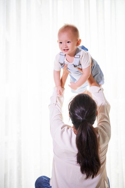 Madre levantando a su niño sonriente cuando juega con él en casa - Foto, imagen