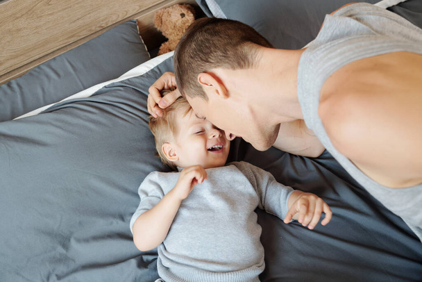 Young father putting child to sleep on his bed, view from above - Photo, Image