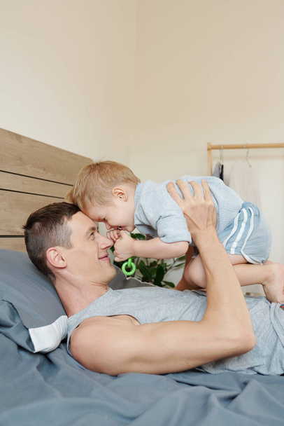 Щасливий батько зі своїм однорічним сином грає вдома на ліжку
 - Фото, зображення