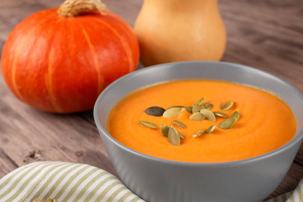 Hokkaido pumpkin cream soup in gray bowl toped with pumpkin seeds on wooden table background with copy space for text. Vegan food concept, homemade soup recipe. Selective focus - Photo, Image