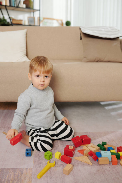 Little boy sitting on the floor and playing with colorful blocks in the room - Фото, изображение