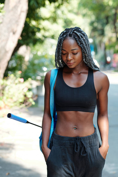 Fit slim young Black woman walking to court with gym bag and badminton racket - Photo, Image