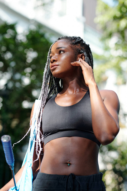 Retrato de una joven negra bastante fuerte con el pelo trenzado caminando a casa después del entrenamiento de bádminton al aire libre - Foto, Imagen