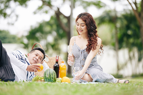 Szczęśliwa młoda azjatycka para w miłości pije wino i je owoce podczas pikniku w parku - Zdjęcie, obraz