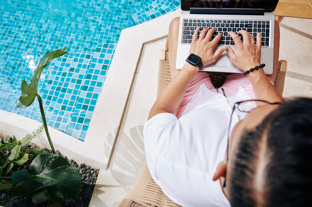 ondernemer zitten bij het zwembad en typen op laptop, uitzicht van boven - Foto, afbeelding