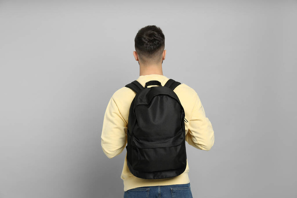 Young man with stylish backpack on light grey background, back view - Foto, afbeelding