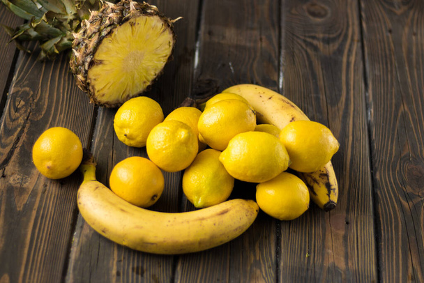 Żółte owoce. Ananas, banany i cytryny na drewnianym tle. - Zdjęcie, obraz