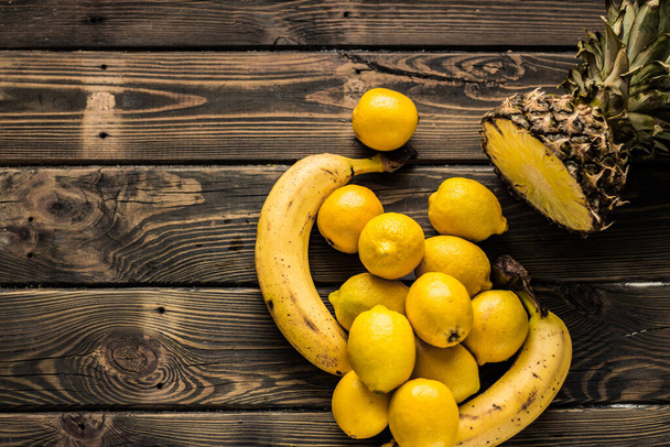 Žluté plody. Ananas, banány a citrony na dřevěném pozadí. - Fotografie, Obrázek