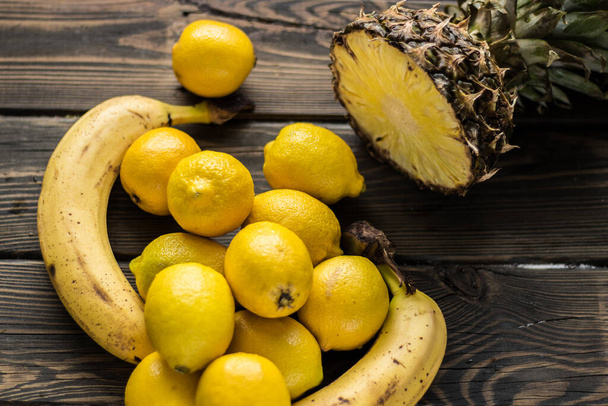 Frutas amarillas. Piña, plátanos y limones sobre fondo de madera. - Foto, imagen