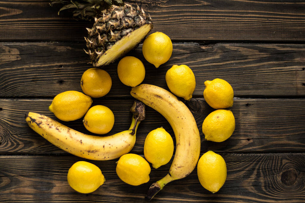Gelbe Früchte. Ananas, Bananen und Zitronen auf Holzgrund. - Foto, Bild