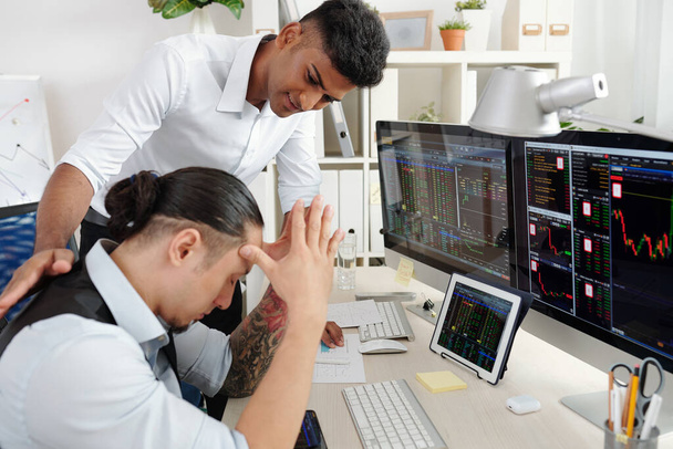 Positive young Indian trader reassuring coworker who lost a lot of money in stock market - Photo, Image