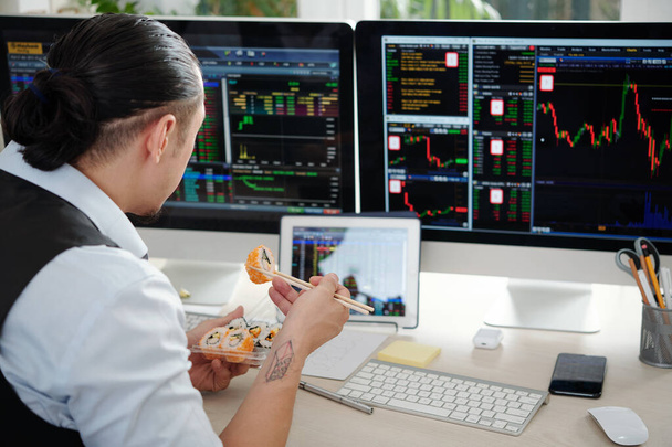 Тревожный финансовый брокер ест суши и анализирует тенденции фондового рынка на компьютерных экранах - Фото, изображение