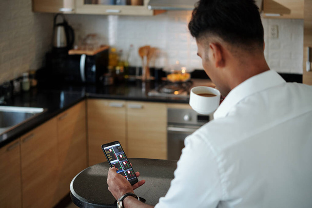Começando investidor bebendo café da manhã e verificando aplicativo de negociação on-line no smartphone - Foto, Imagem