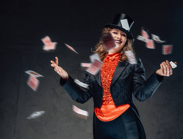 Αστεία γυναίκα απατεώνων από τσίρκο ποζάρει με ιπτάμενες κάρτες σε σκούρο φόντο - Φωτογραφία, εικόνα