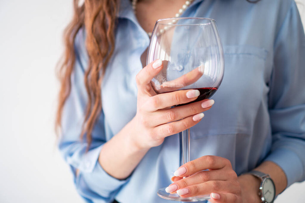 Ofis kızı mavi gömlekli ve inci kolyeli, bir bardak şaraplı. - Fotoğraf, Görsel