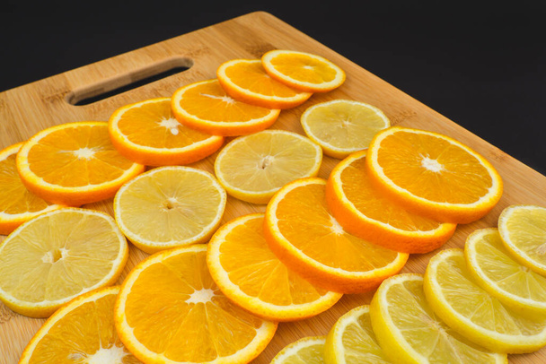 Κομμάτια από λεμόνια και πορτοκάλια σε μια ξύλινη σανίδα. Κοντινή εικόνα φρούτων σε μαύρο φόντο - Φωτογραφία, εικόνα