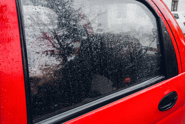 Машина под дождем. Капли дождя на окне красной машины - Фото, изображение
