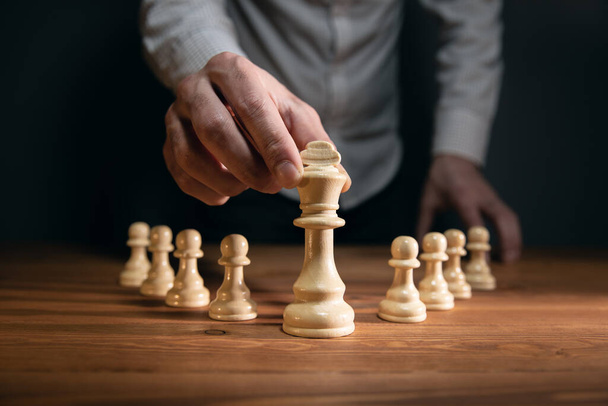 hombre de negocios con las manos dobladas planeando una estrategia con piezas de ajedrez sobre una vieja mesa de madera. - Foto, imagen