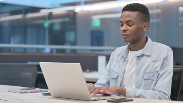 Vonzó afrikai férfi Nézi a kamera használata közben Laptop az irodában - Felvétel, videó