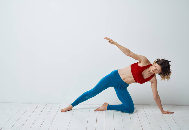 Femme pratiquant le yoga dans une pièce lumineuse et leggings bleus T-shirt rouge - Photo, image