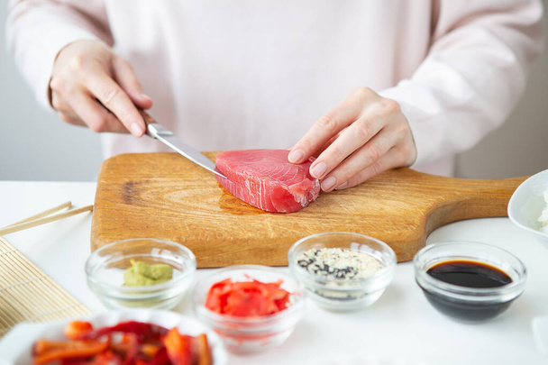 Die Zubereitung von Sushi, die Zubereitung aller Zutaten für Sushi, das Mädchen schneidet den Thunfisch - Foto, Bild